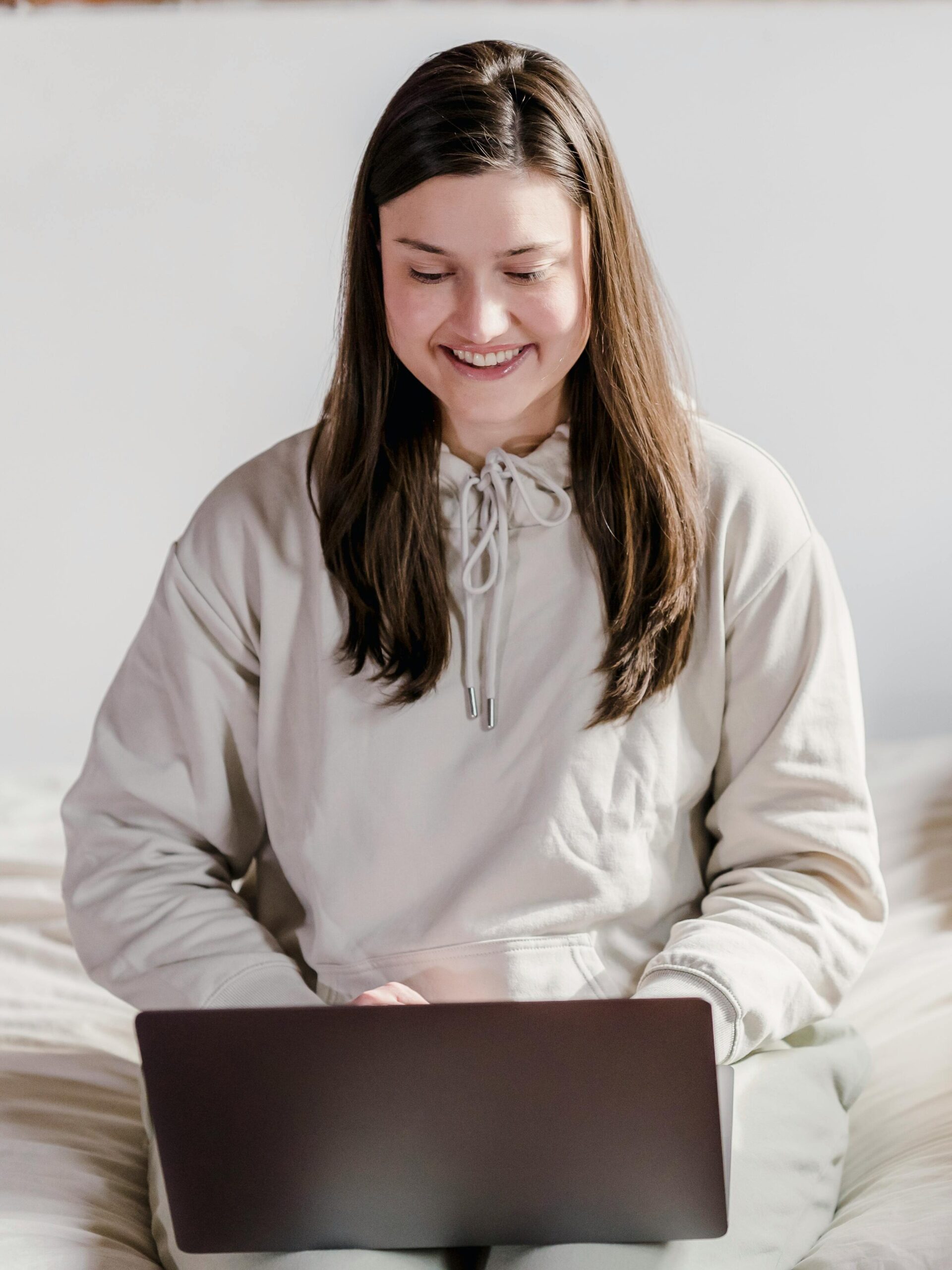 A cheerful woman using a laptop in a cozy bedroom with plants.