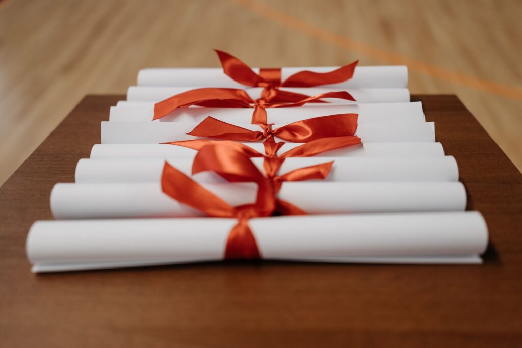 ¿Vale la pena hacer una maestría? Close-up of rolled diplomas tied with red ribbons on a wooden desk, ready for presentation.